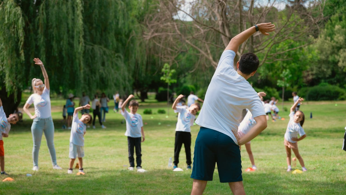 Children and instructors stretching in a park during a summer physical education class.